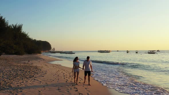 Hand-held couple in love enjoying first rays of sunny day, walking on exotic beach washed by sea wav alt