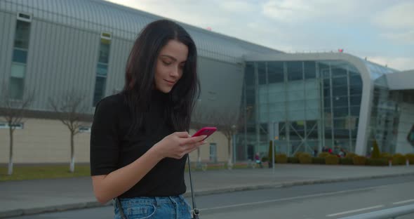 Beautiful Girl Is Smiling and Texting on the Phone When Standing Near the Airport. She Is alt