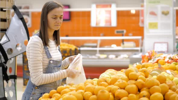 Young Woman in Denim Overall Is Selecting Fresh Oranges at Grocery Store