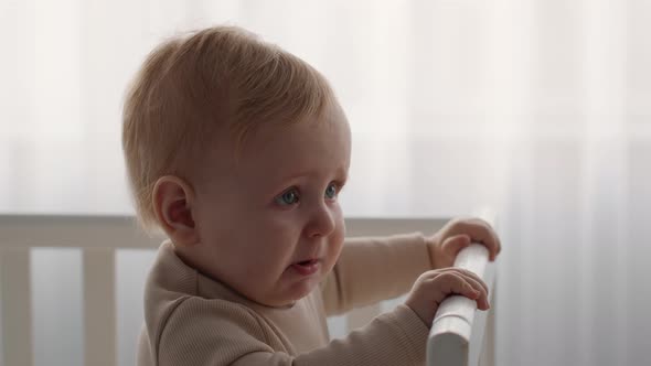 Closeup Of Adorable Infant Child Standing In Baby Bed At Home alt
