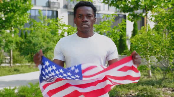 Zoom in Afroamerican Man Holding an American Flag Looks Camera and Says USA alt