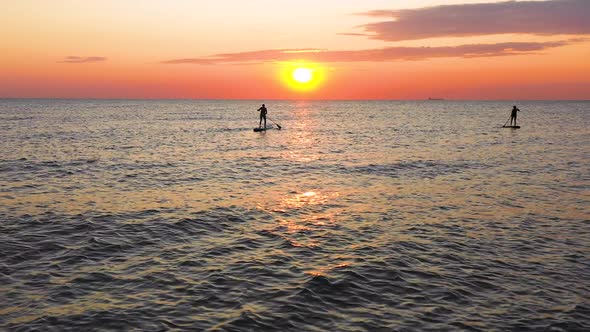 Two stand up paddlers enjoy tropical island sunset in the ocean. Travel concept alt