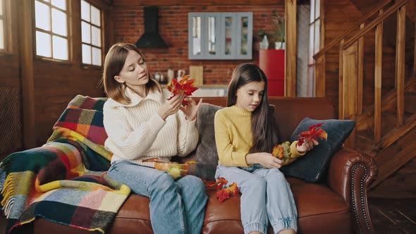 Young Mother and Little Daughter are Decorating Pumpkin with Orange Autumn Leaves Laughing and alt