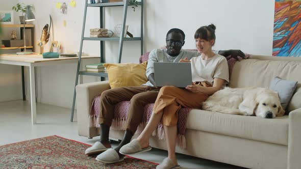 Multiethnic Family Couple Using Laptop and Talking in Living Room alt