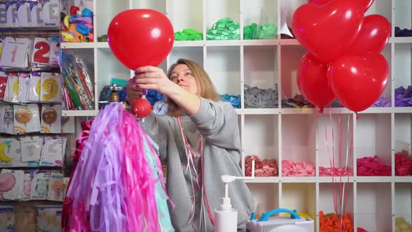 a Woman Inflates of Helium From a Balloon in the Shape of a Heart alt
