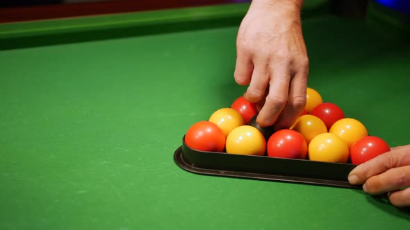 A man setting up the pool balls on a table in a triangle. He spins the eight ball alt