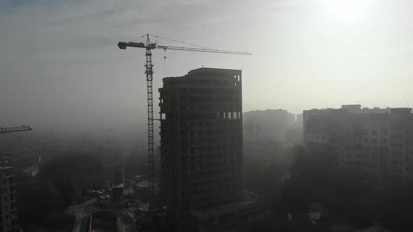 Birds eye view on tower crane in fog standing next to residential building.