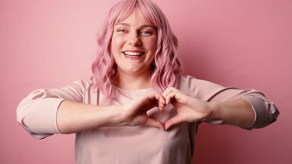 Beautiful Young Girl Showing Heart with Fingers Symbol of Love Looking at Camera Isolated on Pink