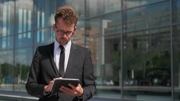 Businessman Working on Tablet Standing Next To Office Building alt