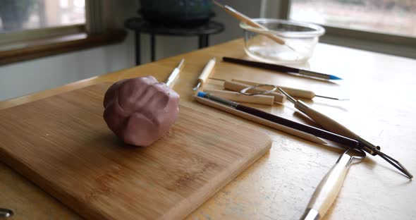 A ball of brown modeling clay for sculpting, tools, brushes and art supplies on a wooden table in an alt