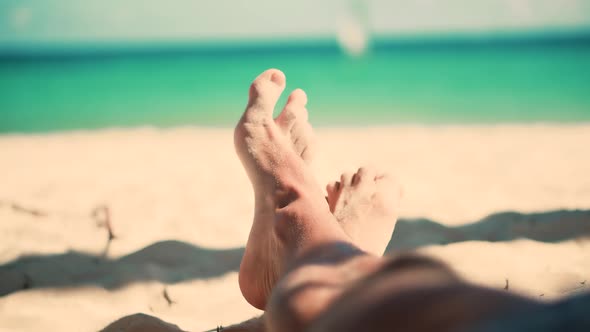 Man Lying On Beach And Moving Legs On Holiday Vacation. Legs Man On Beach Sun Lounger Sandy Shore. alt