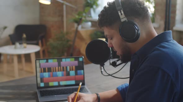 Podcaster Putting on Headphones and Writing on Speech on Paper alt