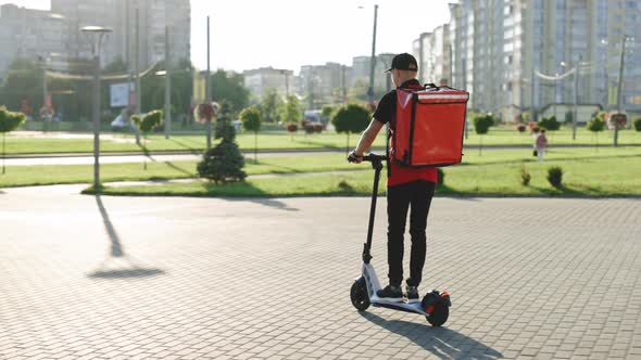 Man Courier Food Delivery With Red Thermal Backpack Rides on an Electric Scooter Deliver Online