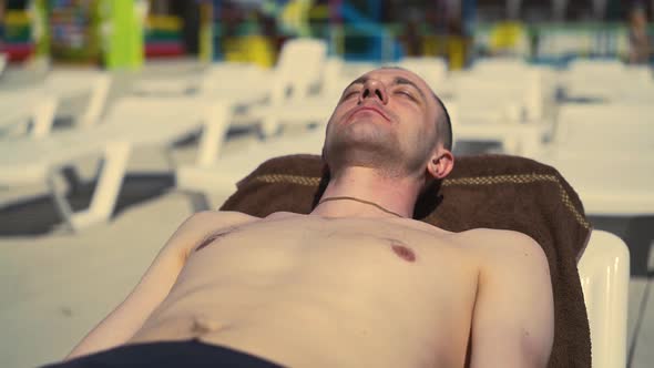 Closeup Bald Italian Man Is Lying on the Beach on Sun Lounger Sunbathing alt