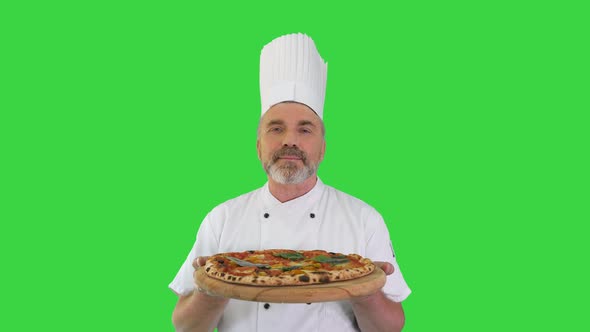 Happy Senior Cook with a Pizza in Hands Looking To Camera on a Green Screen Chroma Key alt