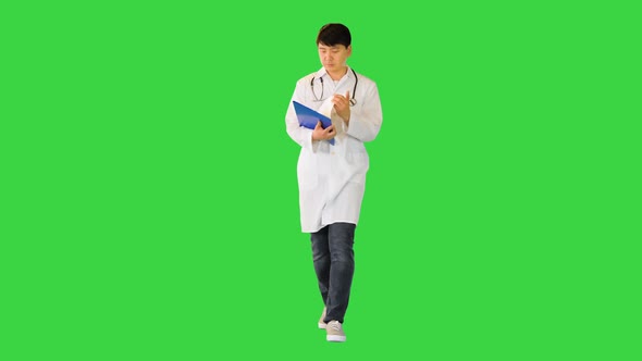 Young Asian Doctor Walks Studying a Document on a Green Screen Chroma Key