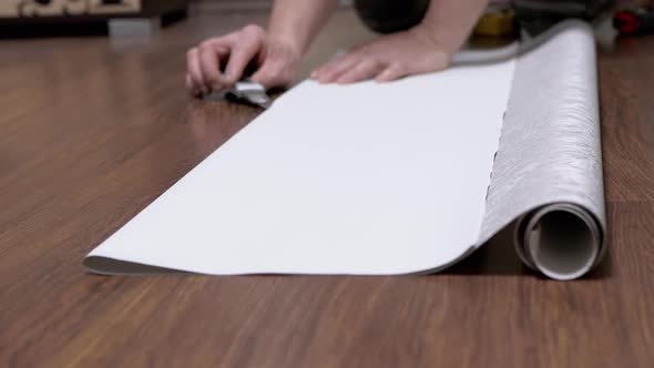 Male Sitting on Floor Cuts Off a Strip of Wallpaper for Pasting with a Knife alt