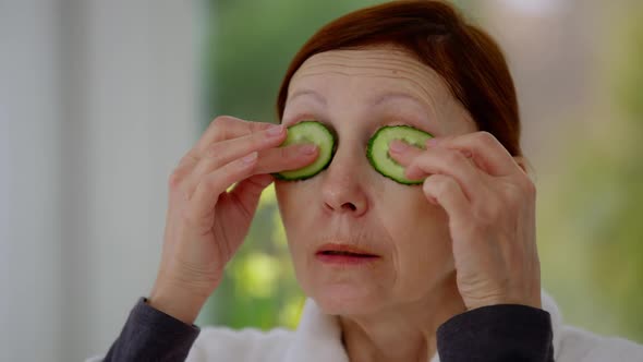 Closeup Face of Mature Caucasian Woman Applying Cucumber on Eyes Looking Away alt