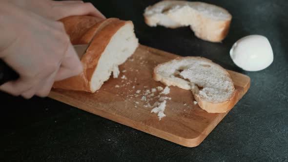 Woman's Hands Cutting a Piece of White Bread on Wooden Board in Black Background