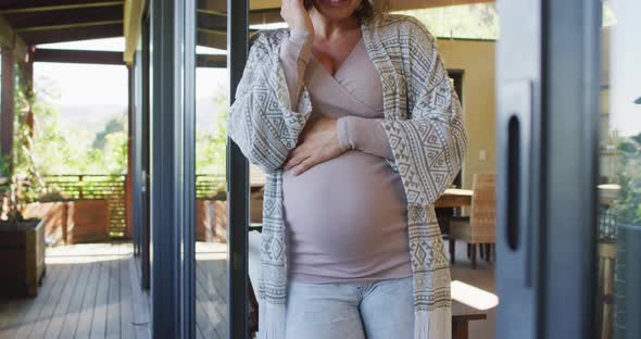 Happy caucasian pregnant woman standing on patio and having phone call alt