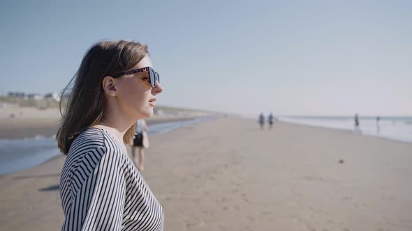 Closeup of a Woman on the Beach Looking at the Ocean on a Windy Sunny Day alt