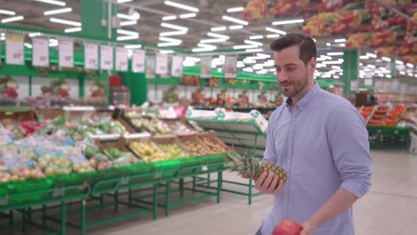 Attractive young man dancing with fresh fruits in supermarket