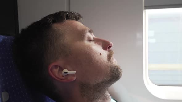 Casual Man with Earphones Getting Some Sleep on Long Train Journey alt