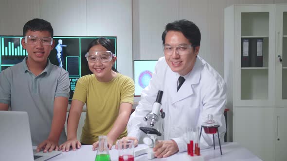 Boy And Girl Learning Science Experiment With Teacher In Classroom, They Smile To Camera alt