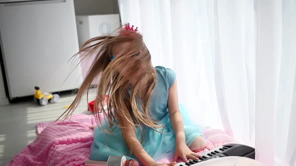 A little girl in a beautiful blue dress glasses plays the synthesizer
