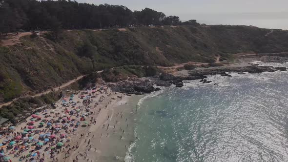 Aerial view over El Canelo beach at Chile on a sunny day with people in the beach's sand alt