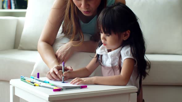 Young mother teaching her daughter painting colour pencil on paper 