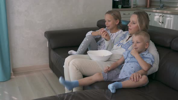 Mom and Two Children Eating Popcorn and Watching TV While Sitting on the Couch