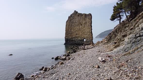 An unusual rock standing in the sea. Flat rock in the form of a sail with a hole in the middle