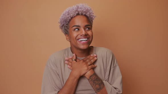Beautiful Excited Blonde Dark Skinned Female Keeps Hands on Chest with Happiness alt