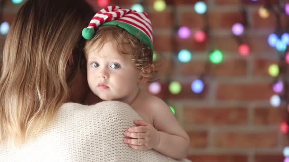 Mother with son in funny hat on color fairy lights background