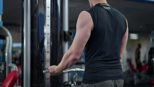 Back View of Unrecognizable Fit Sportsman Training Biceps on Exercise Machine in Gym alt