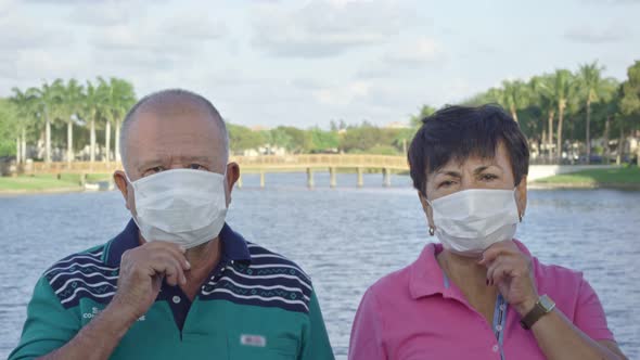 Elderly Couple Looking at Camera While Taking Face Masks Off in Front of Lake alt