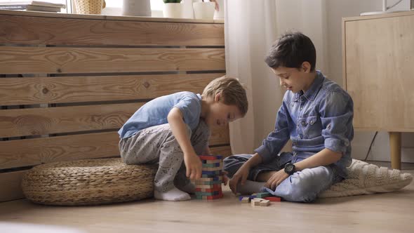 Two Boys Brothers Are Building a Tower From Wooden Blocks Sitting on the Floor