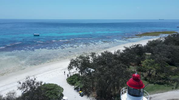 Unique lighthouse looking over a tropical reef surrounded by shades of blue water. Moving drone view alt