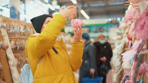 Woman in Yellow Winter Jacket Choosing Christmas Ornament on Christmas Market in Shopping Mall alt