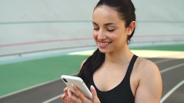 Sporty Girl Using Mobile Phone at Stadium. Ssport Woman Checking Results alt