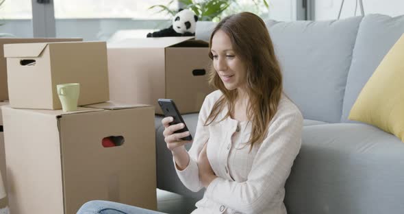 Woman moving in her new home and using her smartphone