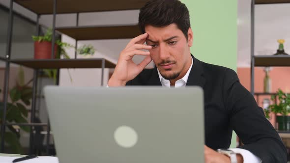 Worried Hispanic Man Sits at the Desk in Front of Laptop in Modern Office Looks at the Screen