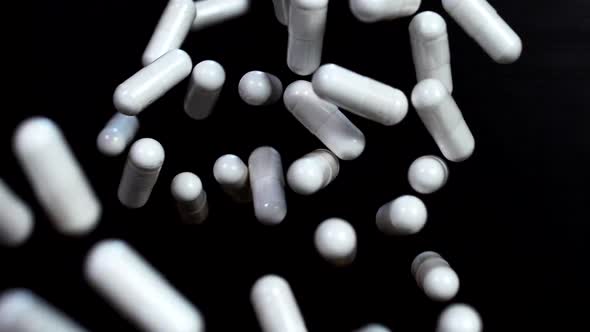White capsules of vitamins fly up and hover in the air in slow motion against a black background alt