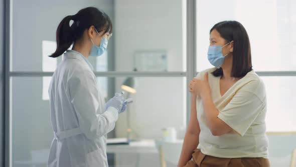 Female Doctor Vaccinating Asian Woman in Clinic alt