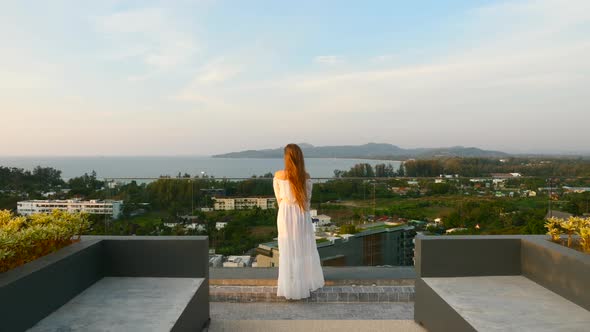 Back View of Alone Woman Standing on Rooftop on Sunset with Seaview alt
