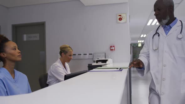 Diverse male doctor coming to hospital reception and talking to female staff alt