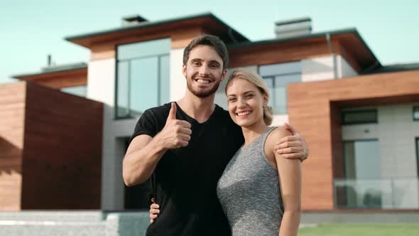 Happy Couple Making Thumbs Up Gesture Near Luxury House alt