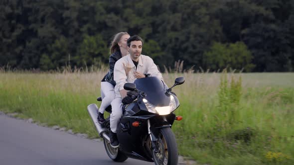 Beautiful Couple Rides Sport Motorcycle on the Road Near Field