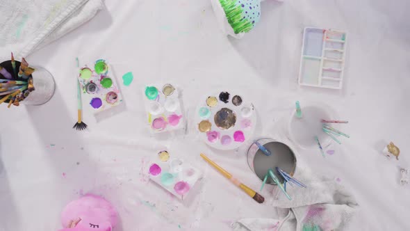 Flat lay. Little girl painting paper mache figurines with acrylic paint  for her homeschooling art p alt